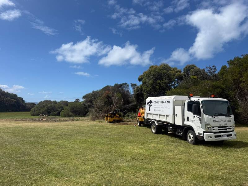 Otway Tree Care truck and chipper on a grassy airfield beside a line of coastal scrub being cleared
